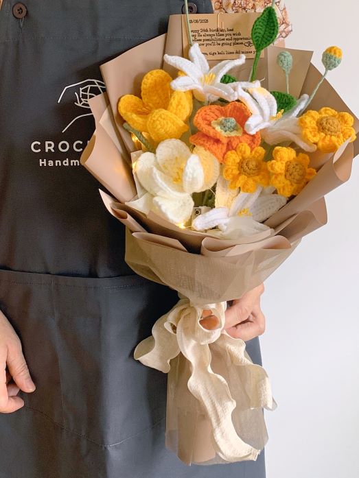 A Lady wearing a CrochetSG.com apron holding a crochet flower bouquet